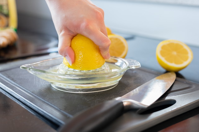 まな板と包丁、ガラスの器具でレモンを絞る手
