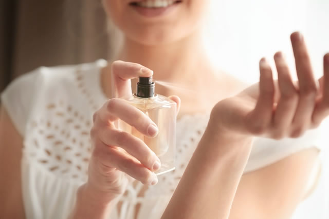 Beautiful young woman with bottle of perfume at home, closeup