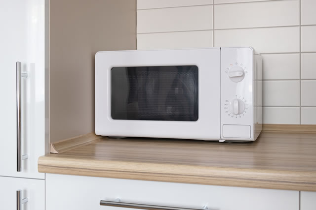 New household appliance microwave oven on wooden tabletop in modern white kitchen. Clean and cozy minimalistic kitchen interior.