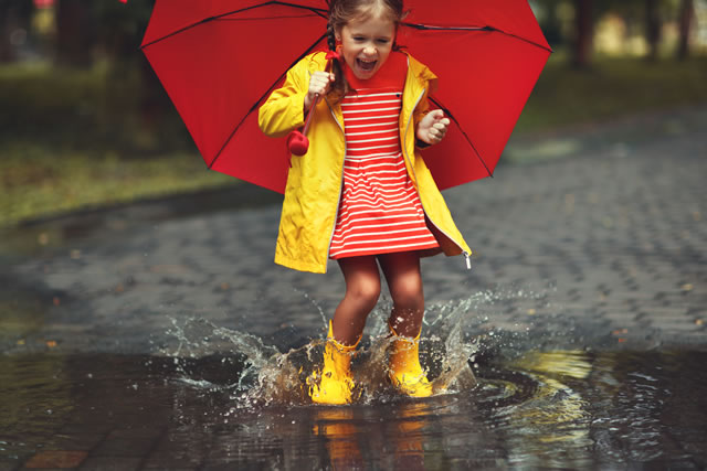 happy child girl with an umbrella and rubber boots in puddle on autumn walk