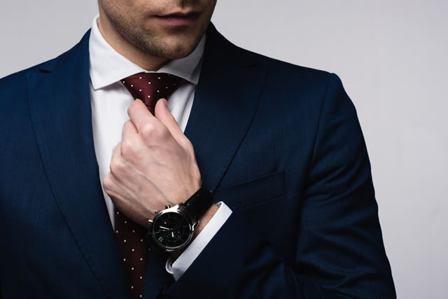 partial view of businessman touching tie isolated on grey