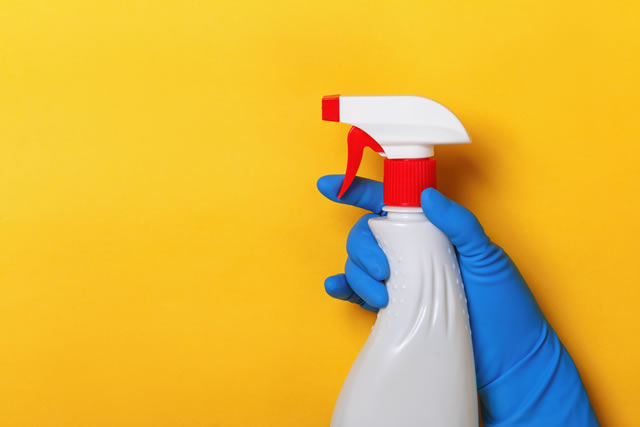 A hand in a latex protective glove holds a spray bottle on a yellow background. Cleaning concept