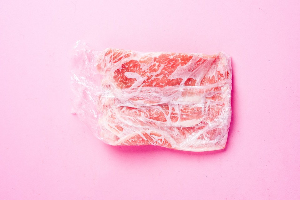 ラップに包んだ冷凍の牛肉、ピンクの背景