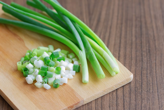 Close up view on chopped fresh spring onion and knife put on wood cutting board on wooden table with copy space. Prepare scallions for cooking. Food and vegetable concept for background or wallpaper.