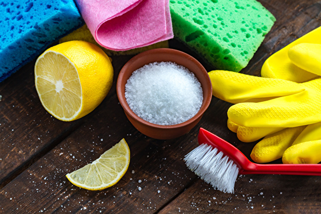 Lemon acid in a small plate, slice of lemon, a juicy lemon, sponge for washing dishes, brushes and yellow rubber gloves for cleaning the house on wooden background. Natural cleaning products