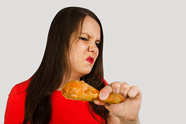 Young pretty woman holds spoiled grilled chicken leg on a light background.