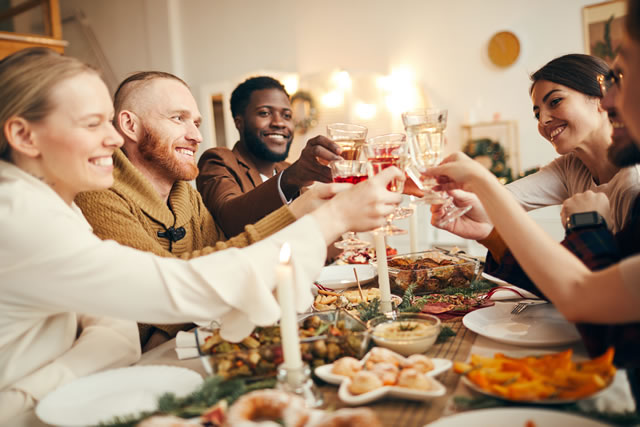 Multi-ethnic group of people raising glasses sitting at beautiful dinner table celebrating Christmas with friends and family, copy space