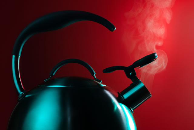Photo of stainless steel kettle in neon light over red background. Steam from the kettle through the whistle.