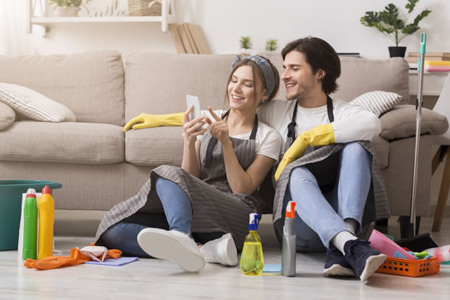 Smiling young couple relaxing with smartphone after cleaning apartment