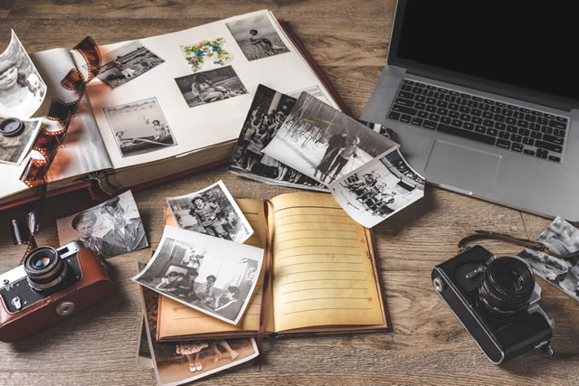 Old family photos and album on wooden background. Vintage pictures, camera, notepad and modern notebook composition.