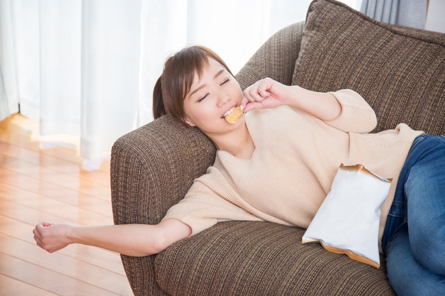 ソファで寝転がってお菓子を食べている女性