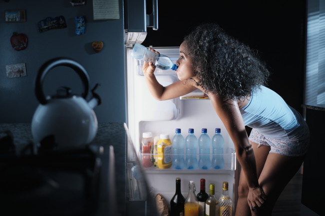 冷蔵庫を開けて水を飲んでいる女性