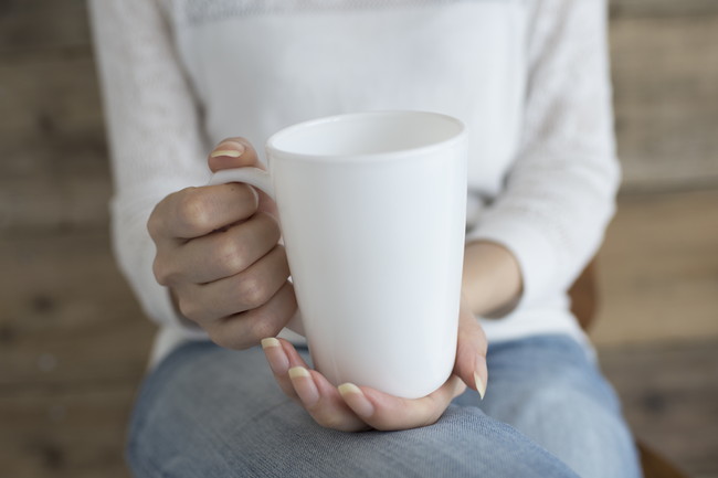 白いコーヒーカップを持って座っている女性