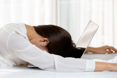 ノートパソコンの上に顔を伏せ疲れている様子の女性