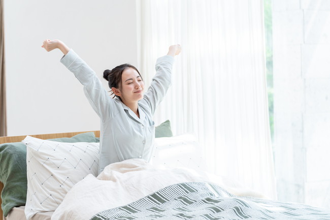 朝ベッドから伸びをしながら起きる女性