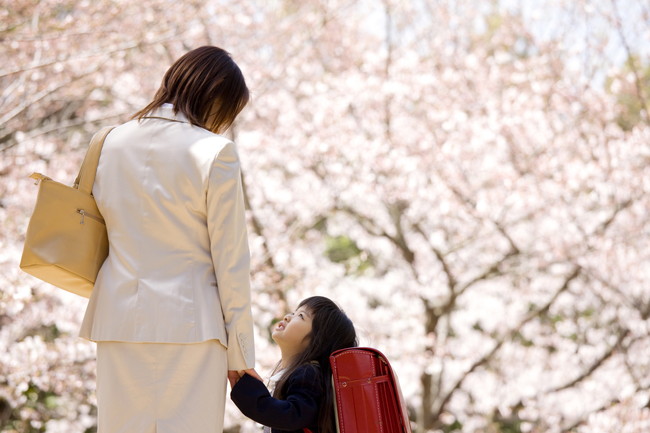 入学式で桜の下で手をつなぐ親子