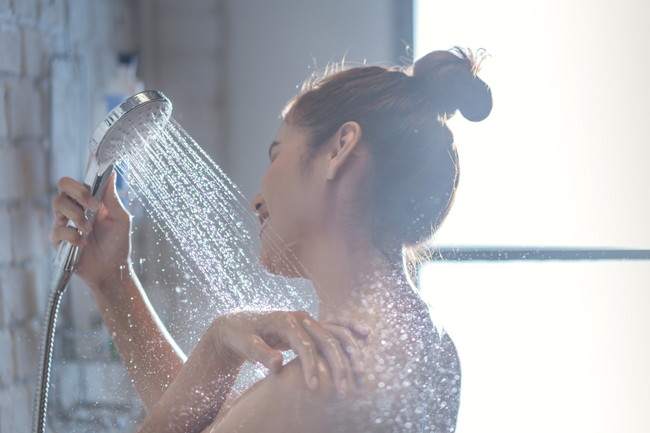 髪を一つにまとめてシャワーを浴びている女性