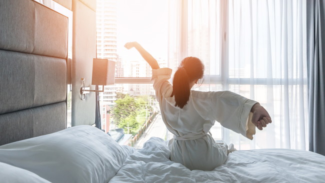 ベッドの上で朝陽を浴びる女性