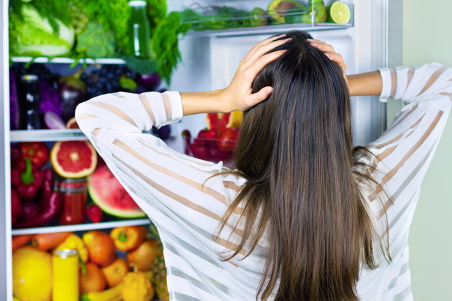 食品が詰まった冷蔵庫と頭を抱える女性