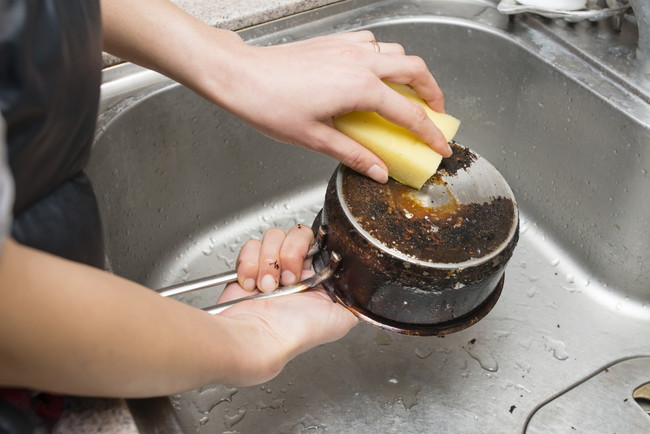 鍋の焦げ付きを磨く女性