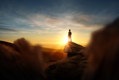 断崖絶壁から朝陽を見ている人の後ろ姿
