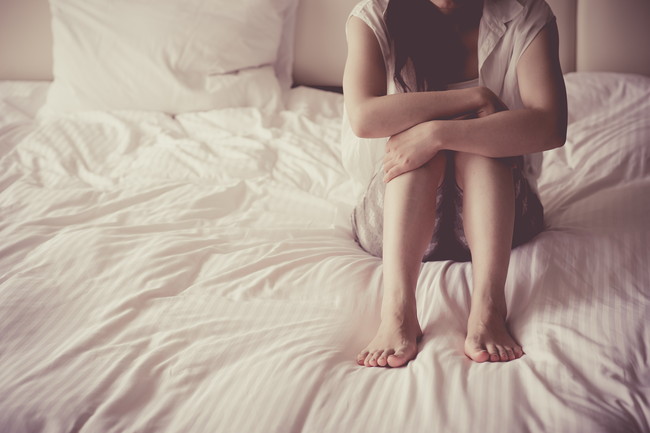 ベッドの上で膝を抱えている女性