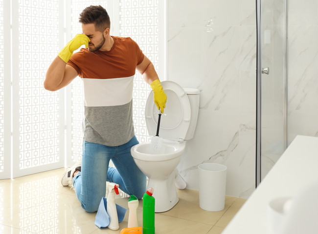 鼻をつまんでトイレ掃除をする男性