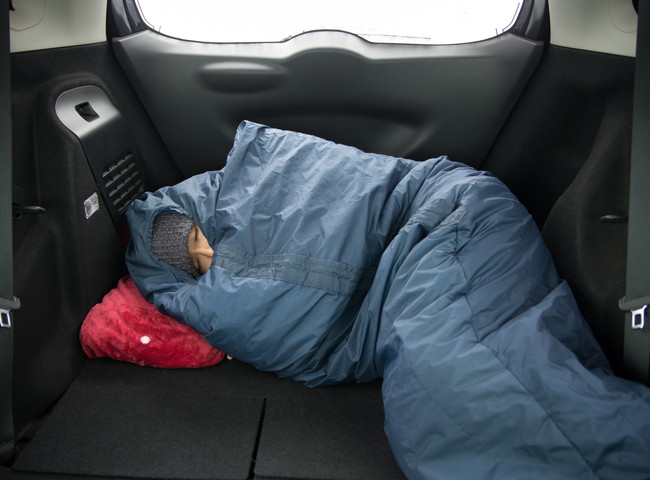 寝袋で車中泊する人