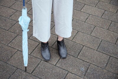 レインブーツと傘を持つ女性の足元