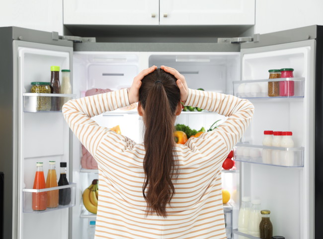 冷蔵庫の中を見て頭を抱える女性