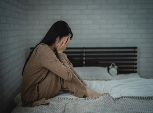 ベッドの上で落ち込む女性
