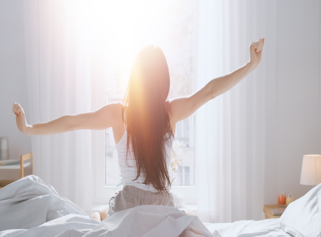 朝日とベッドの上の寝起きの女性