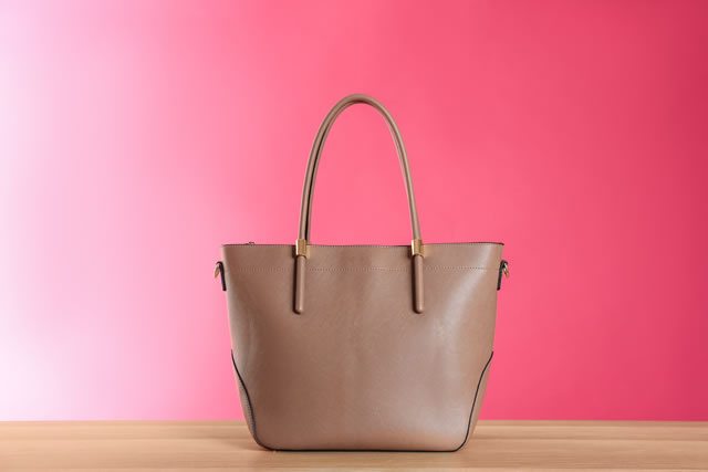Stylish woman's bag on wooden table against pink background