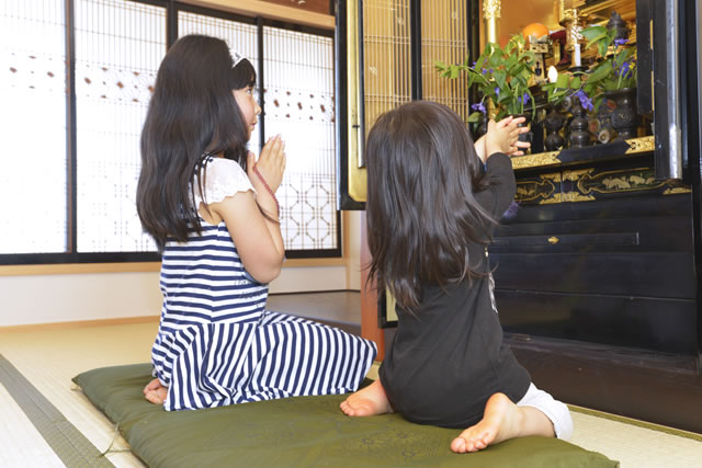 仏壇の前に座って合掌している子どもたち